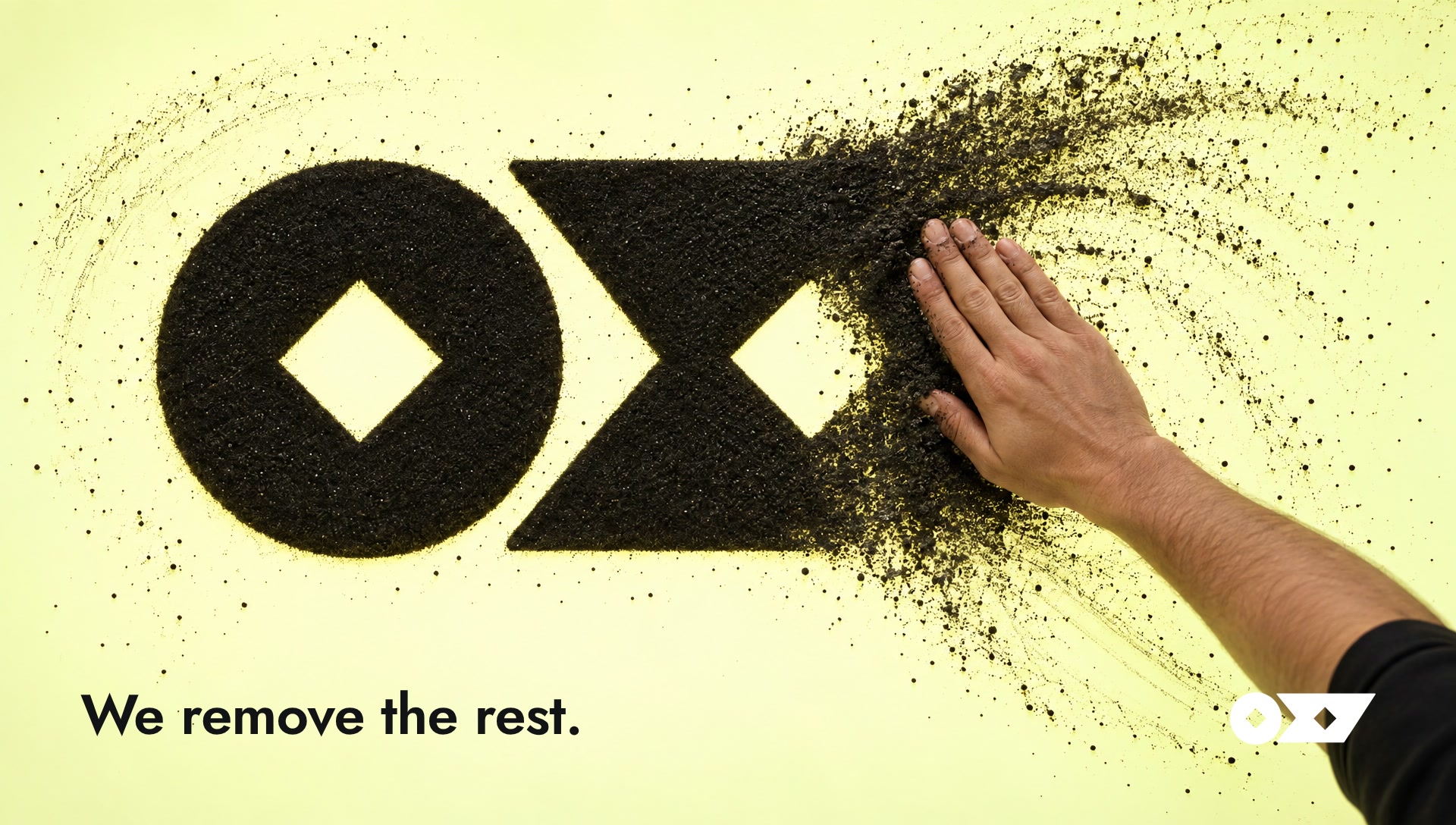 Key art: a hand sweeping black sand to reveal the Oxy mark on a glowing table